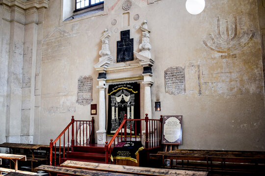 Interior of a historic synagogue with an ornate Torah ark, wooden pews and Hebrew inscriptions