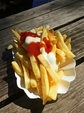 Fast food: french fries topped with mayonnaise and ketchup on a wooden table outside