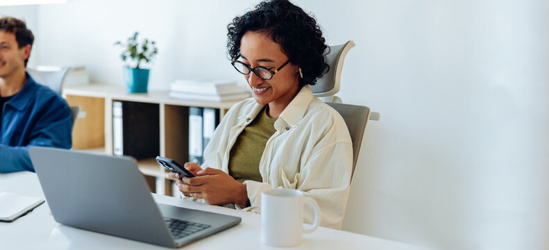 Woman at office work using phone and laptop