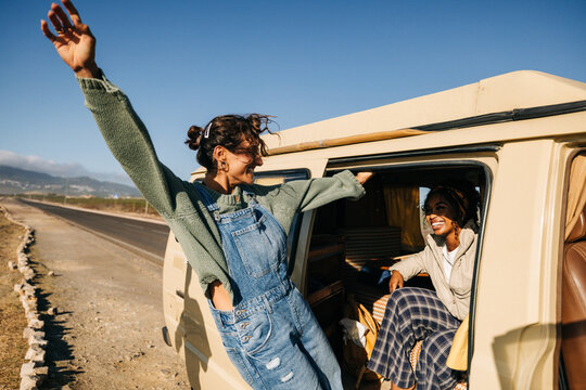 Joyful friends enjoy a road trip adventure with a woman leaning from a van window