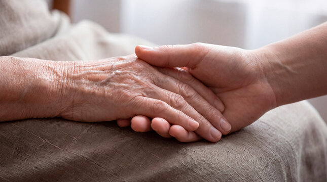 Adult daughter tenderly holding her elderly mother's hand in a quiet living room