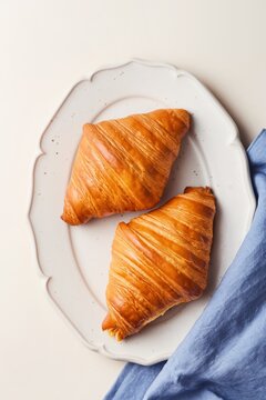 Freshly baked croissants on a decorated beige plate with a blue tea towel. Top view