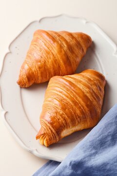 Freshly baked croissants on a decorated beige plate with a blue tea towel