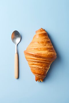 Croissant with a tea spoon on a blue background. Top view