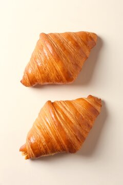 Fresh croissants laying on a flat beige surface. Top view