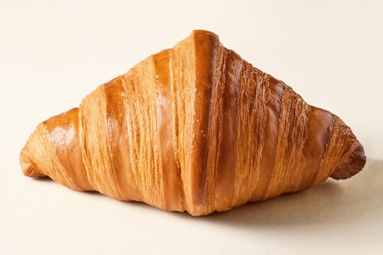 Fresh croissant laying on a flat beige surface viewed from the side