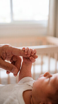 Tiny newborn baby holding onto a parent's finger while lying peacefully in the crib
