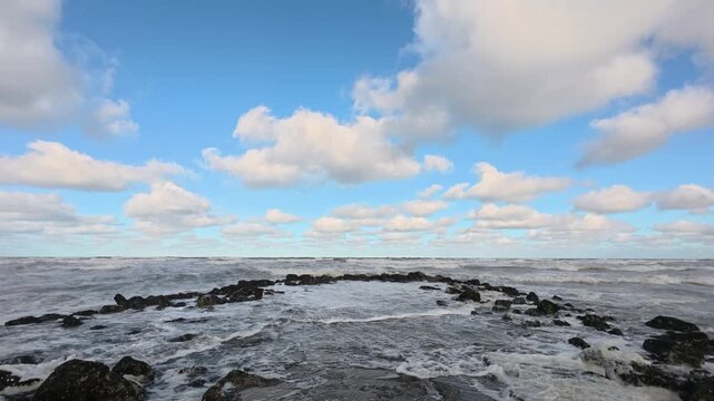 Dramatic seascape with powerful ocean waves breaking against a rocky shore under a cloudy blue sky.
