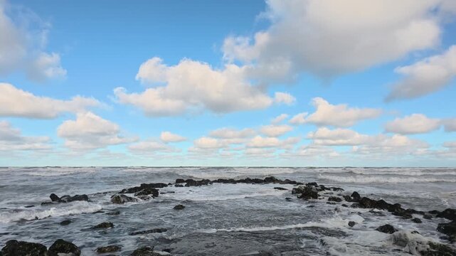 Dramatic seascape with rough ocean waves crashing on a rocky shore under a beautiful blue sky with clouds.