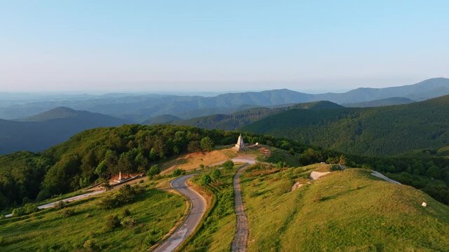 Aerial view Shipka Pass Balkan mountains green hills winding path sunset golden hour Shipka Monument background Bulgaria travel tourism hiking destination landscape drone