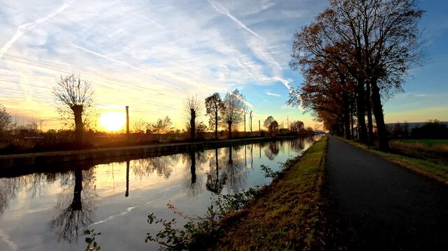 Serene Autumn Sunset over a Calm Canal with Tree Reflections and a Picturesque Walking Path