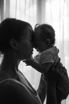 ilhouette of a mother lifting her baby up in front of a window, cozy home atmosphere. Black and white photo