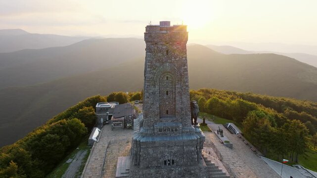 Aerial view Shipka Monument Liberty stone tower sunset golden hour light mountain peaks background Shipka Peak Bulgaria travel destination historical memorial hiking drone
