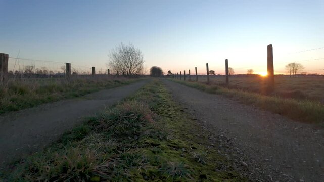 Cinematic crane shot revealing a tranquil country road at sunrise, showing a path leading into the golden light.