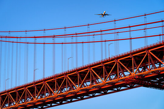 The suspension bridge on April 25 in Lisbon against blue sky with TAP Air Portugal plane flying overhead, Portugal.