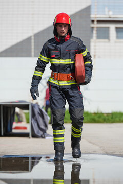 Male Firefighter In Full Gear Carrying Hose During Training Drill With Reflective Puddle
