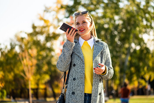 Stylish and beautiful businesswoman using smartphone while walking outdoor in autumn, combining professional work, communication and modern urban lifestyle.