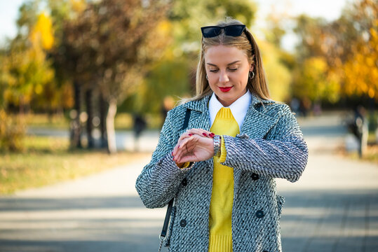 Elegant businesswoman takes a moment to check the time while walking through a city park filled with beautiful autumn colors.