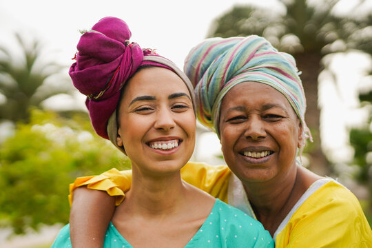 Happy african mother and daughter smiling on camera wearing traditional clothes and turban outdoor - Family love, culture and bonding concept - UGC content
