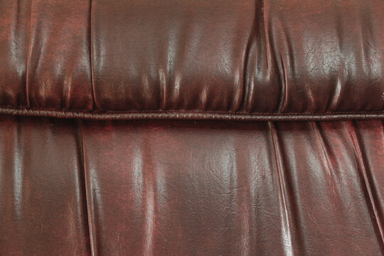 Dark reddish brown faux leather upholstery texture with deep creases and stitched seam.