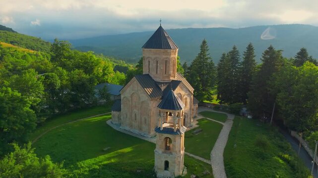 Picturesque aerial perspective of the historic nikortsminda cathedral, a georgian orthodox church surrounded by lush green forests and mountains during a beautiful sunny day in the racha region