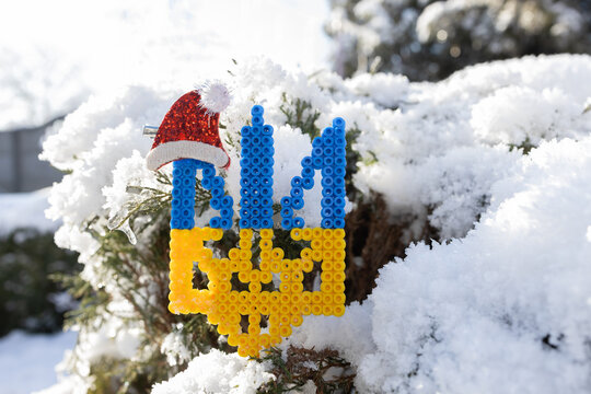 blue and yellow Ukrainian trident with a small red Santa hat on a snow-covered tree. Symbolic Christmas decorations for Ukraine. Stand with Ukraine.