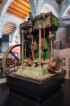 Large antique industrial marine steam engine with flywheel and mechanical components displayed in a historical museum hall.