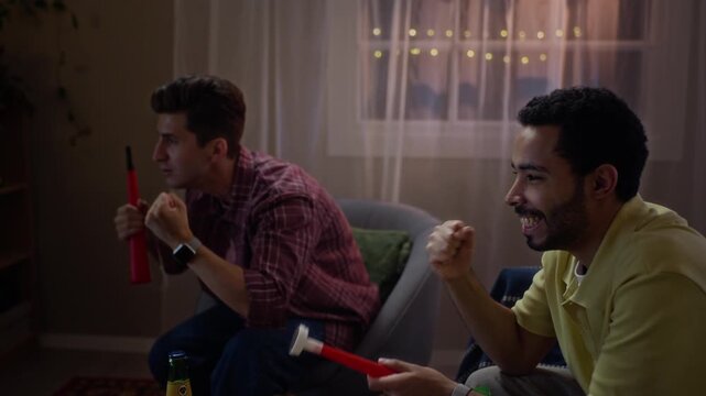 Multiethnic young adult male fans watching sports game at home, cheering with noisemakers. Ideal for sports broadcast advertising, streaming service campaigns, and fan engagement promotions