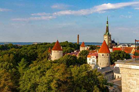 Breathtaking panoramic view of Tallinn Old Town in warm sunset light. Scenic medieval cityscape with fortress towers, St Olaf church spire, and Baltic sea under a golden evening sky.