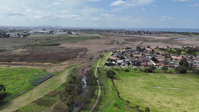 Aerial view of Laverton Creek meandering past residential housing, open parkland, and coastal wetlands in Altona Meadows, with the distant Melbourne city skyline and Port Phillip Bay on the horizon.
