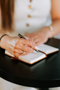 Young woman writing with a pen in a small journal while sitting at a round black wooden table