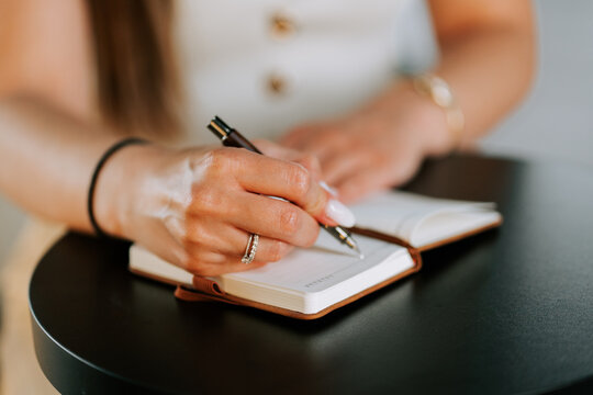 Woman writing in a notebook with a pen while sitting at a dark round table during the daytime