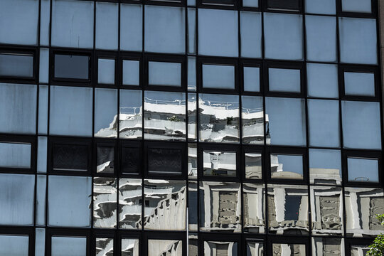 Abstract modern architecture with a blue glass facade and geometric windows distorting the reflection of a building across the glass surface in daylight