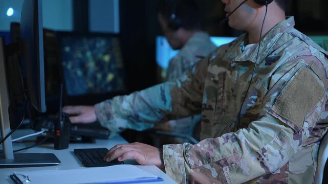 Military operator with headset analyzes radar HUD screens and takes notes in high tech command center