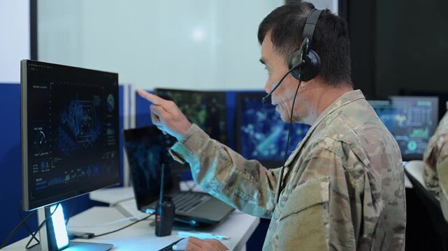 Senior military officer in camouflage uniform uses a computer and headset to analyze cyber intelligence and surveillance data
