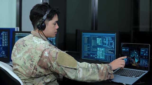 Military operator with headset analyzes radar HUD screens and takes notes in high tech command center
