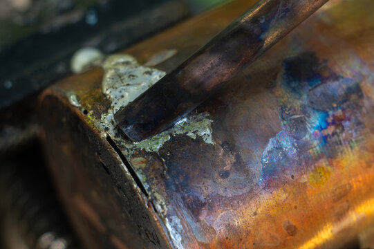 Close-up of copper pipe soldering joint on metal surface with molten solder and heat marks. Plumbing repair and brazing work. Metalwork craft and pipe fitting technology concept