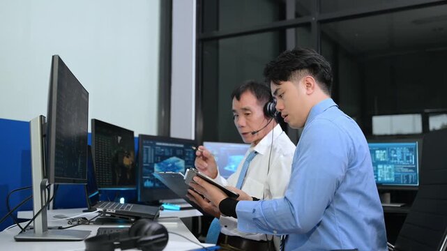 Two Asian male operators analyze global shipping and harbor data on digital screens. Teamwork