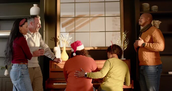 Diverse family and friends gathering at home by upright-piano players starting carol
