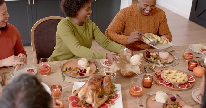 Family and friends placing roll basket, passing dishes and serving turkey at home table celebrating