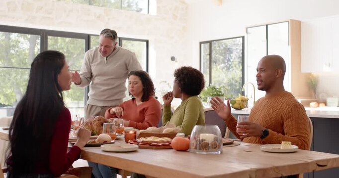 Diverse group sitting at home table for meal standing man speaking carving turkey others listening