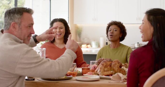 Diverse family at table with turkey reacting as man gesturing, reaching for phone sharing picture
