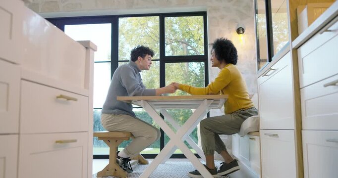 African American men in turtleneck at table by window holding hands while talking