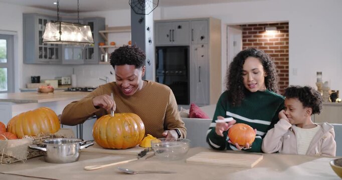 African American family removing lid, scooping seeds and carving pumpkin at kitchen island to carve