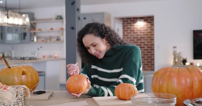African American woman in green top selecting pumpkin making fall decor with white pen in kitchen