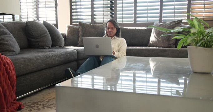 Mature woman working on laptop at home on floor, moving laptop aside, rubbing forehead from fatigue