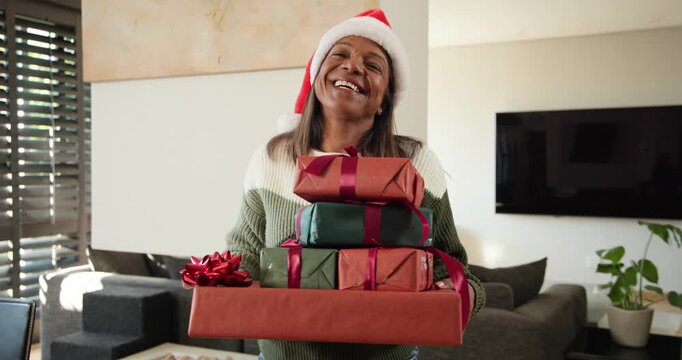 African American female holding gifts, in Santa hat for holiday, smiling, tilting as camera rolling