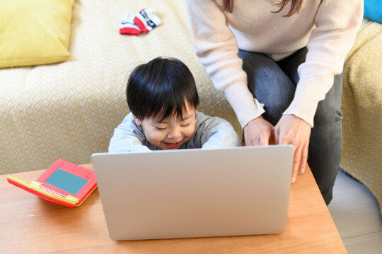 Japanese mother teaching toddler son to use a laptop at home