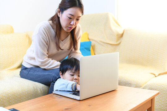Japanese mother teaching toddler son to use a laptop at home
