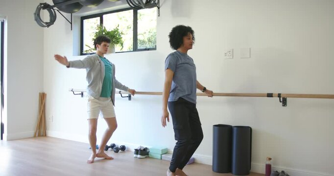Male workout partners performing barre at home gym, front leader starting synced squats for balance
